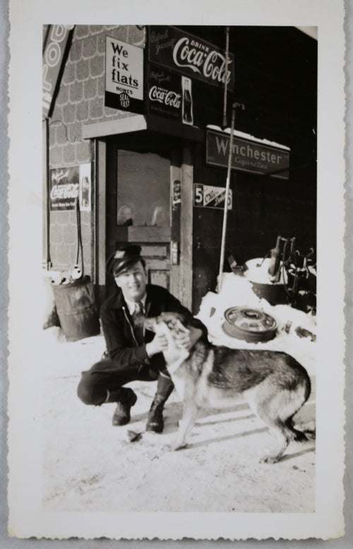 Photo of man and his dog, on front of gas station with ads ~1940s